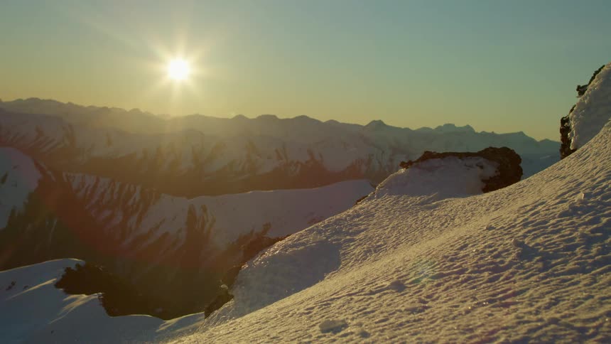 Snow blowing across a mountain as the sun shines down