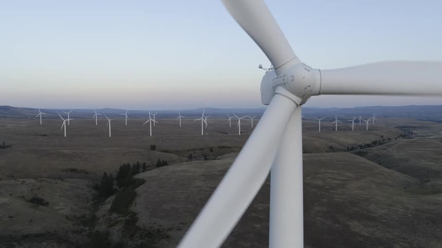 Ascending up the mast of a wind turbine spinning along the foothills of a large wind farm