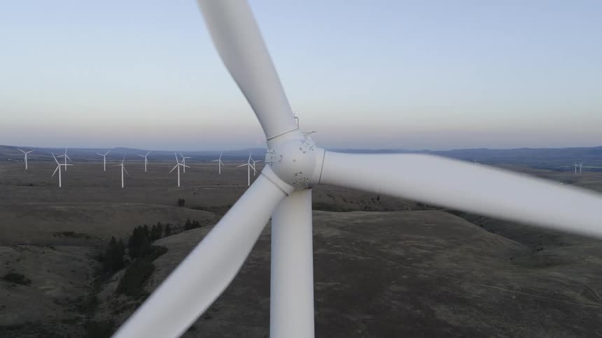 Straight on close up of a spinning wind turbine with rolling hills and other turbines in the distance