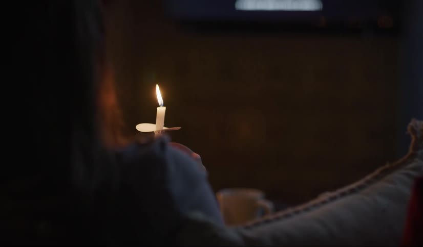 Woman sitting in a couch holding a vigil candle while watching television at night