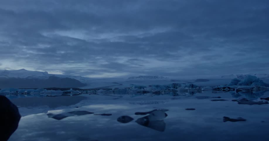 Chunks of ice float in water surrounded by a frozen landscape on a cloudy day