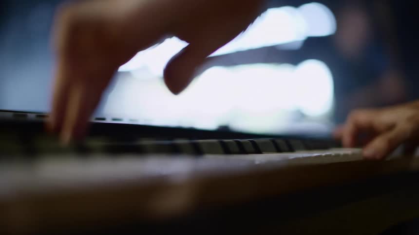 A musician plays keyboard in a well lit room with large windows