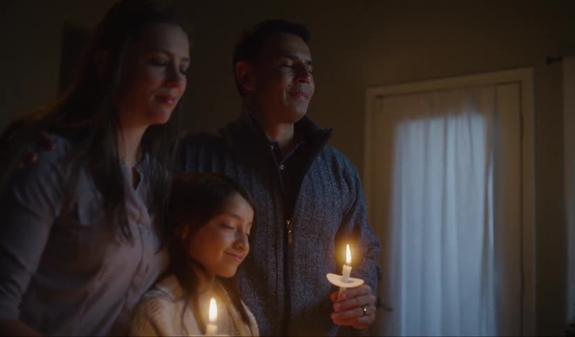 A family hold candles standing in front of a christmas tree