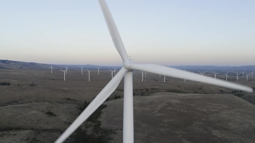 Pullback from close to the blade hub to reveal the entire turbine working on a wind farm