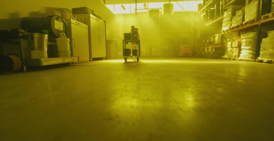 A person in a warehouse pushing a cart with wheels with a wall in the background