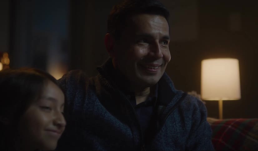Father smiles to his daughter while watching tv at home at night