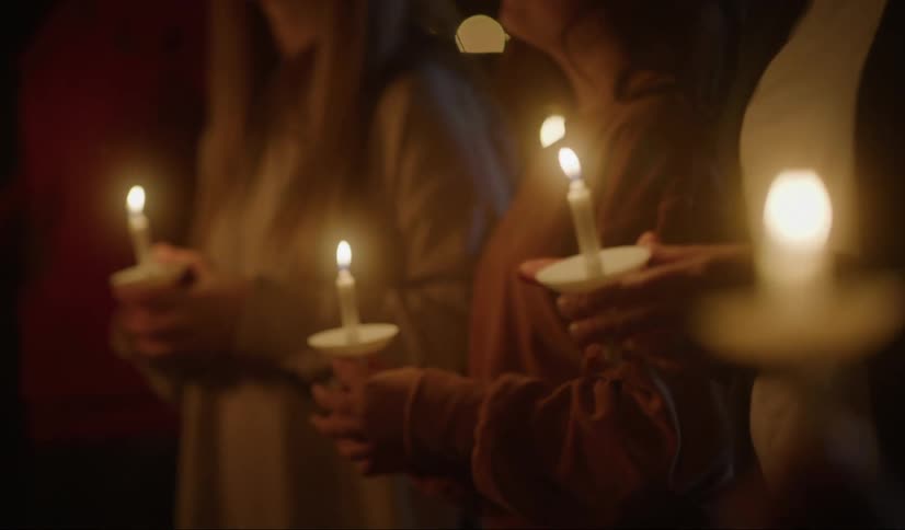 People stand vigil holding lit candles in dark area