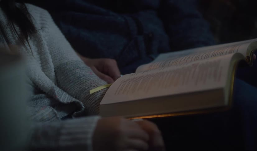 Two people in a room sitting on a couch looking at a book