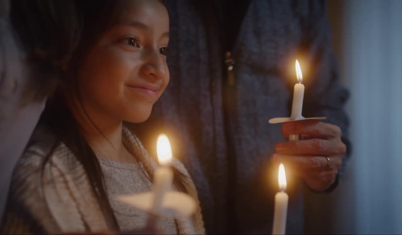 A girl smiles serenely standing between her parents holding a flaming candle