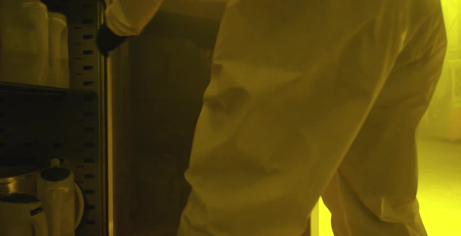 A person in a lab with gloves and a hazmat suit taking a container from a cabinet