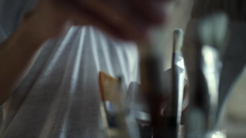 A woman selects painting brush from a stand and takes out two