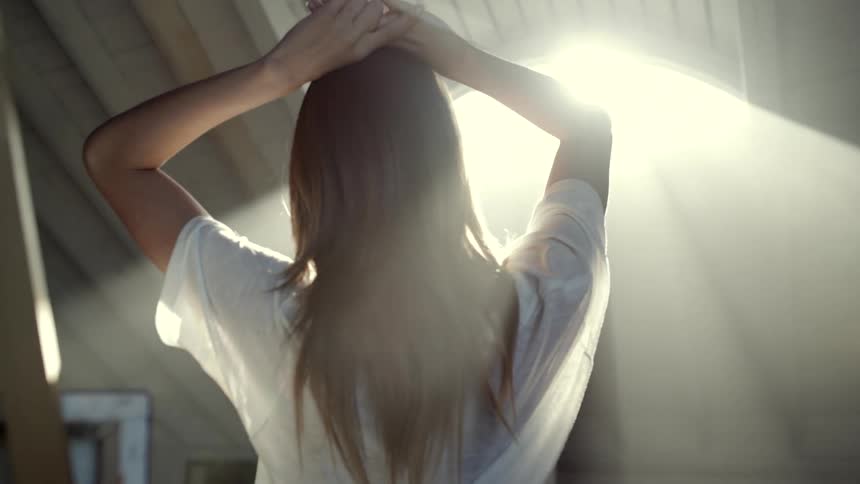 Artist stands with hands on her head under bright glaring sunlight shining from skylight