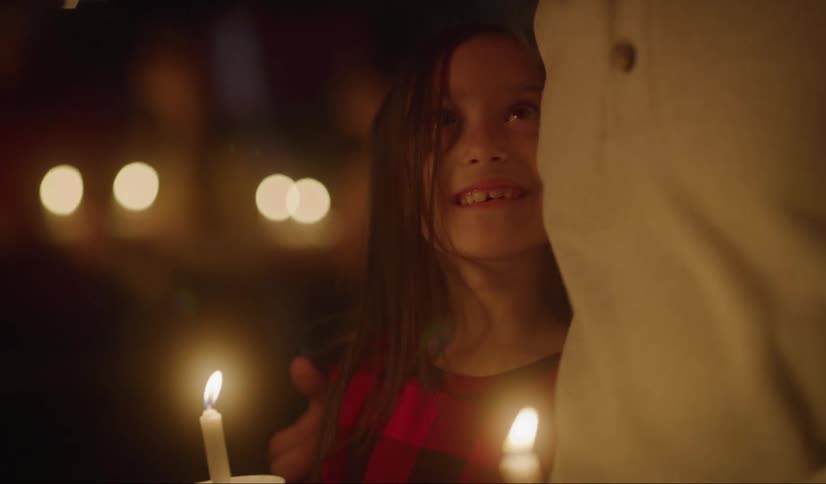 Girl holding a candle being hugged by her dad on a vigil at night