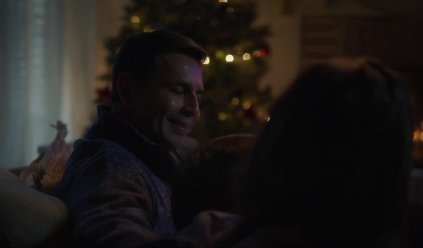 Couple sitting on a couch in the living room next to a christmas tree in front of the fireplace at night