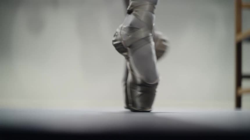 Ballerina dances on point across stage to fellow dancer and chair