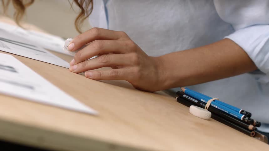 A woman sitting at a drawing table draws and corrects her drawing with an eraser