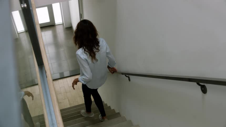 A woman walking down a staircase while holding on to the handrail with a door and a wall in the background