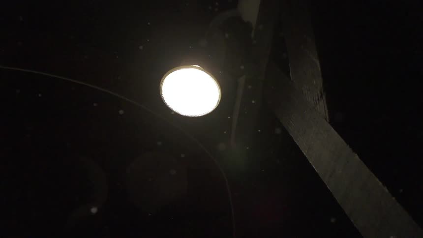 Snow falls under a street light