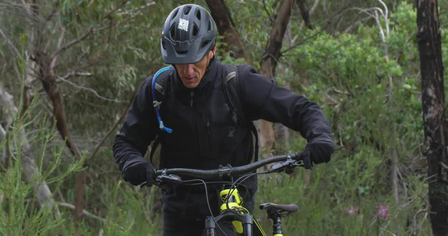 A cyclist pushes a mountain bike through a woodland during the day