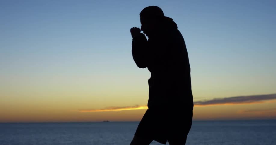 The silhouette of a man shadow boxing with the ocean and golden sky behind him