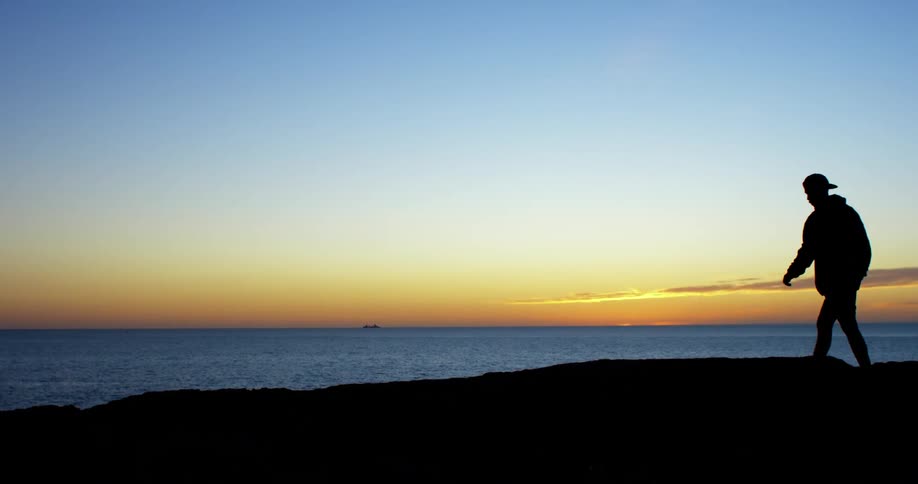A man is walking on the coast of the beach at dusk