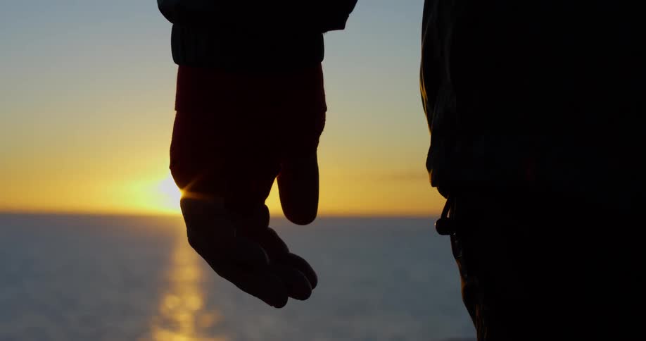 Silhouette of the hand of a man standing in front of the ocean at sunset