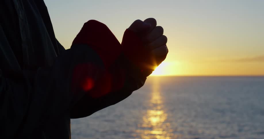 A person meditating with their hands next to the ocean