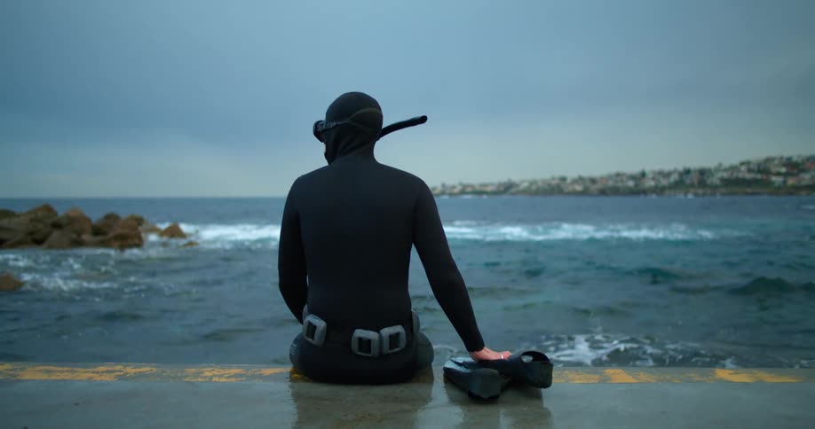 A snorkeler sits on wall looking out at the ocean