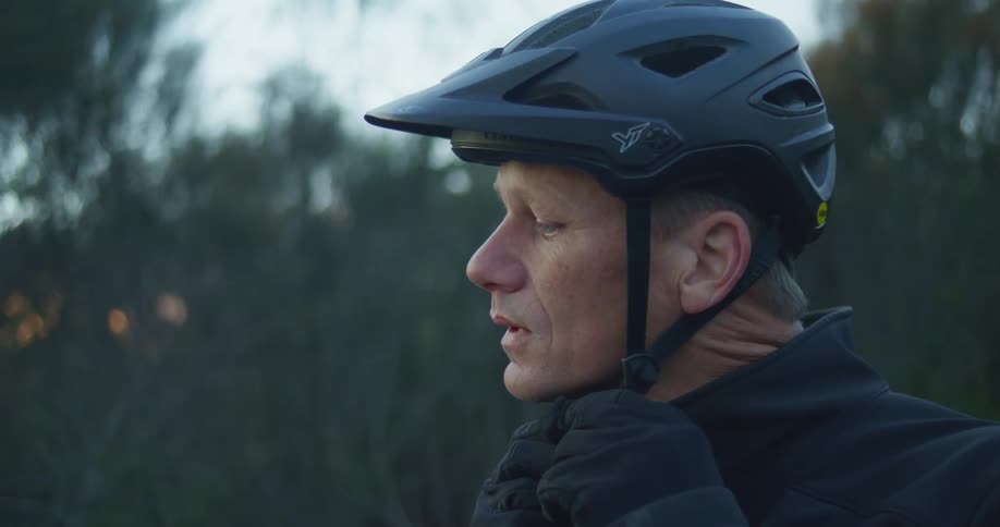 A man is adjusting his helmet outdoors at dusk