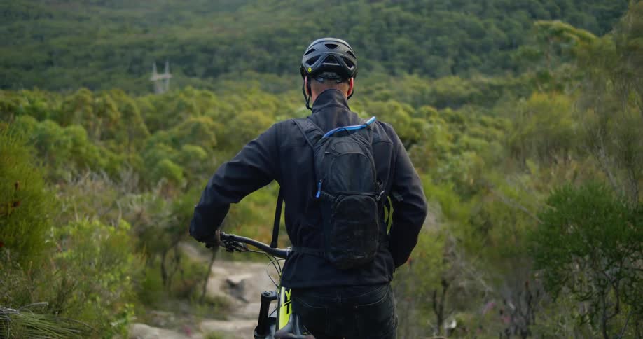 A view of a man standing outside on a trail with a mountain bike