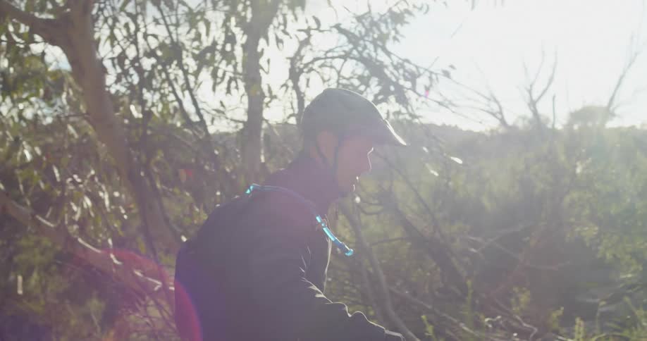Man wearing a helmet carries a bycicle on a trail in the hills