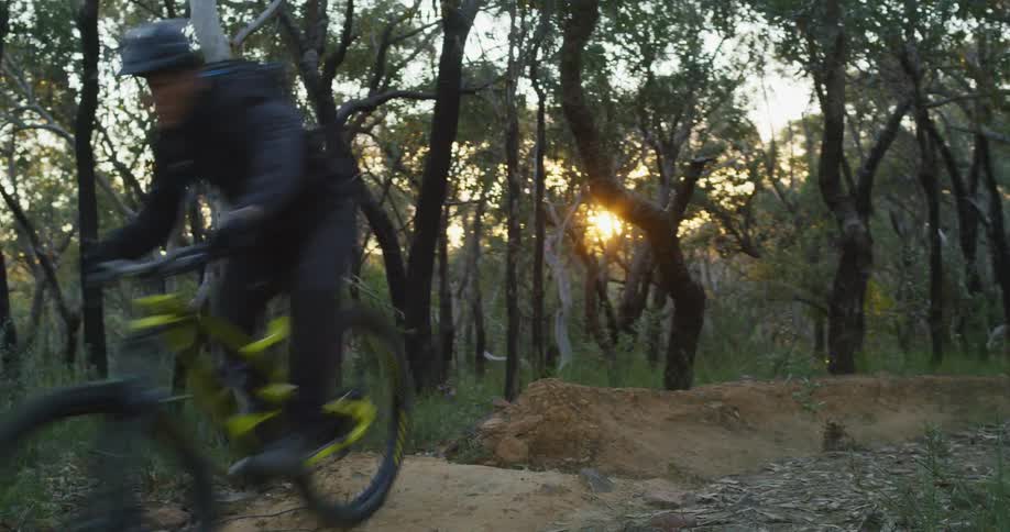 A man with a helmet riding a bicycle on a dirt path in a forest with the sky and clouds in the background