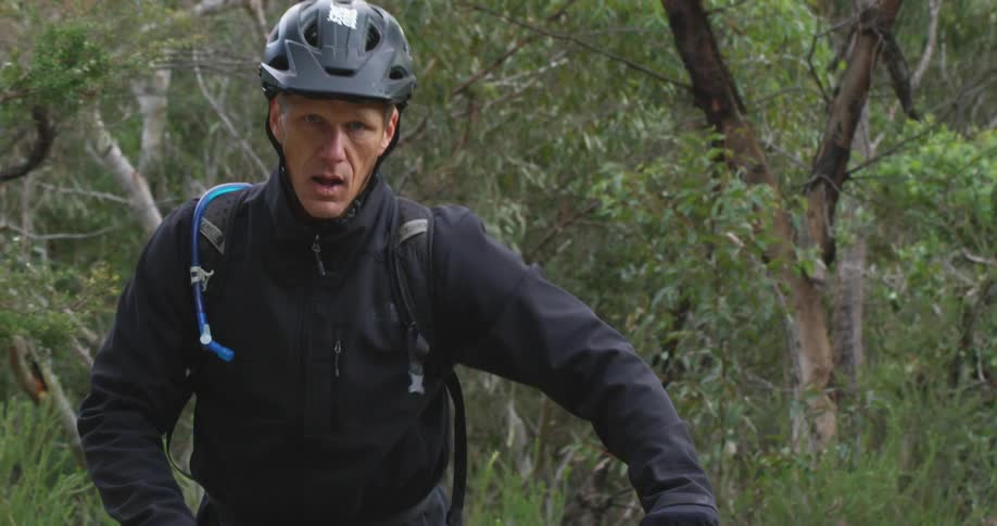 A man pants as he walks his mountain bike up a slope in the woods