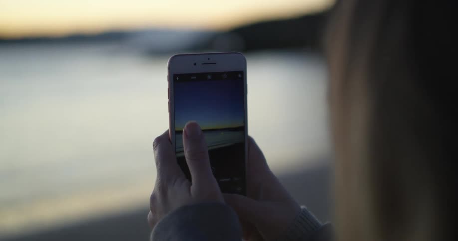 A woman is using her phone to take a picture of a body of water