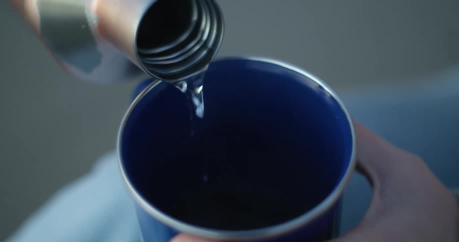A person fills a cup from a thermos