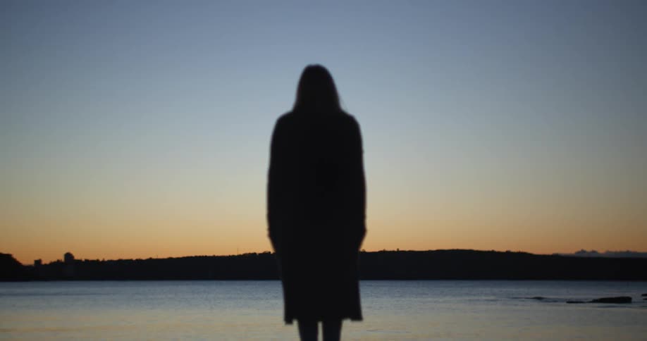A woman looks out over a lake as she stands on the shore at sunset