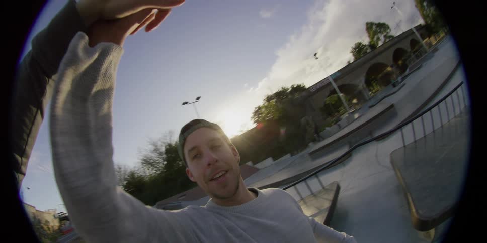 Skateboard approaches fish eye camera giving person a high five