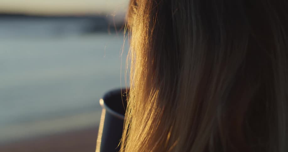 A woman stares out over the water while sipping from a cup