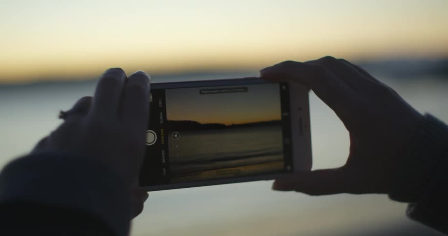 Hands hold up a phone that is taking pictures of the water landscape