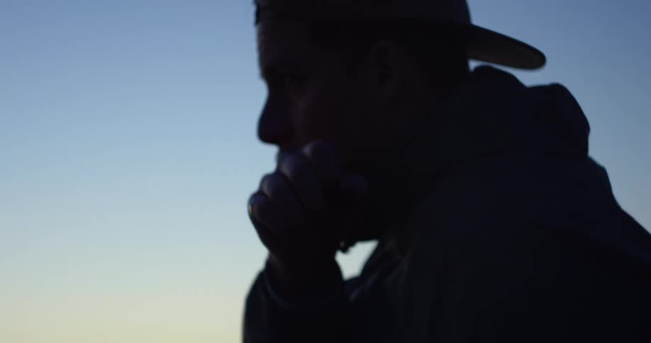 A man with a hat shadowboxing with the sky and clouds in the background