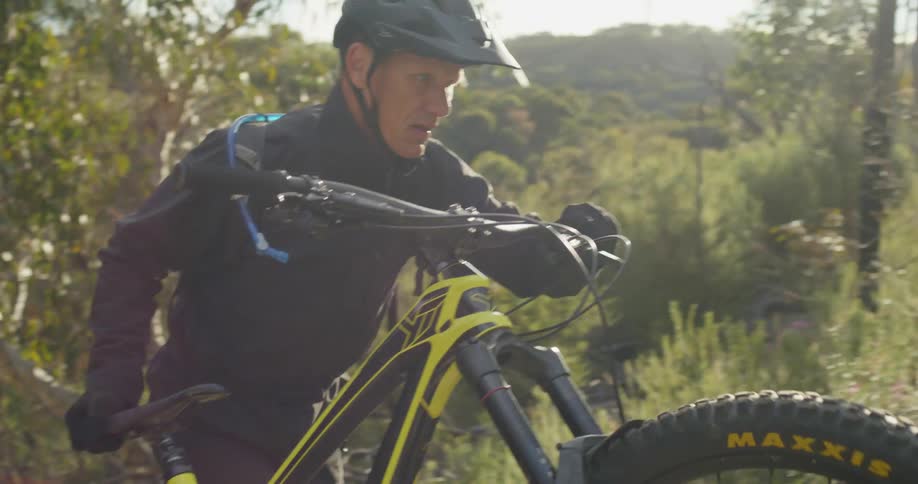 A man turns and lifts his mountain bike to walk it up a slope