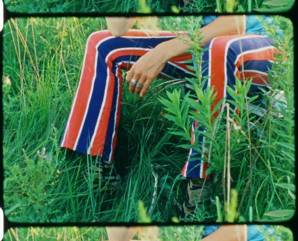 A woman with rings on her fingers sitting on the ground with grass and plants