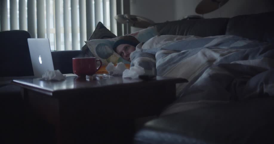 Young sick man resting on the couch in the living room watching movies on a laptop