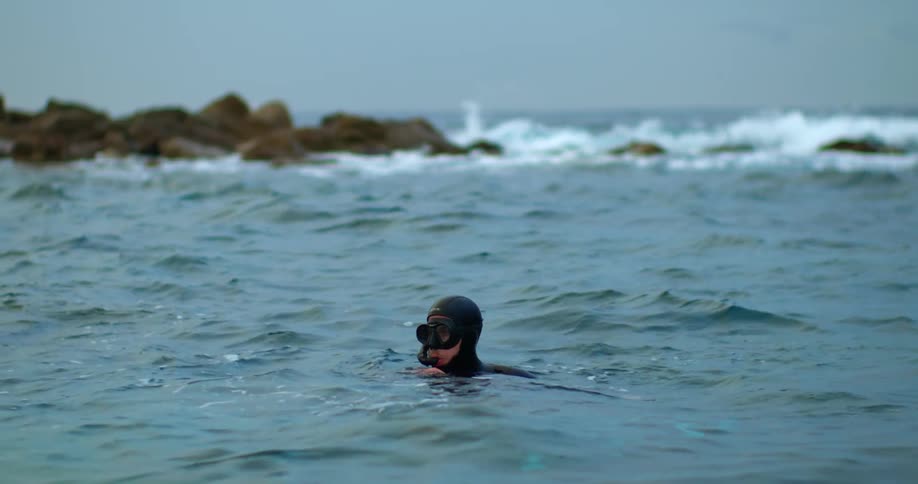 A person in a wetsuit snorkeling on a beach