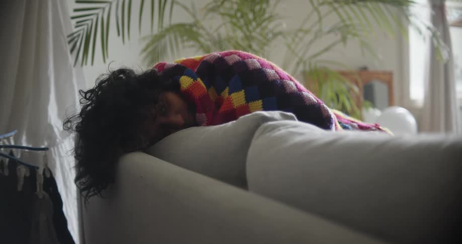 A woman is resting on the couch with a blanket