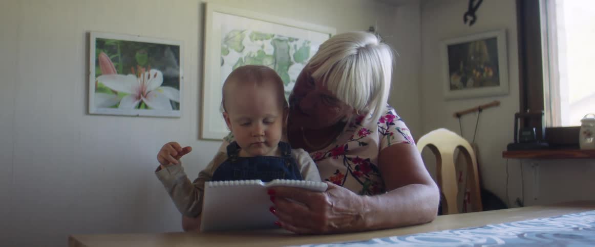 A woman and a child sit at a table looking through a book together