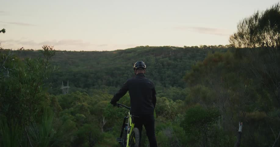 A man is sitting on his bike in a forest at dusk