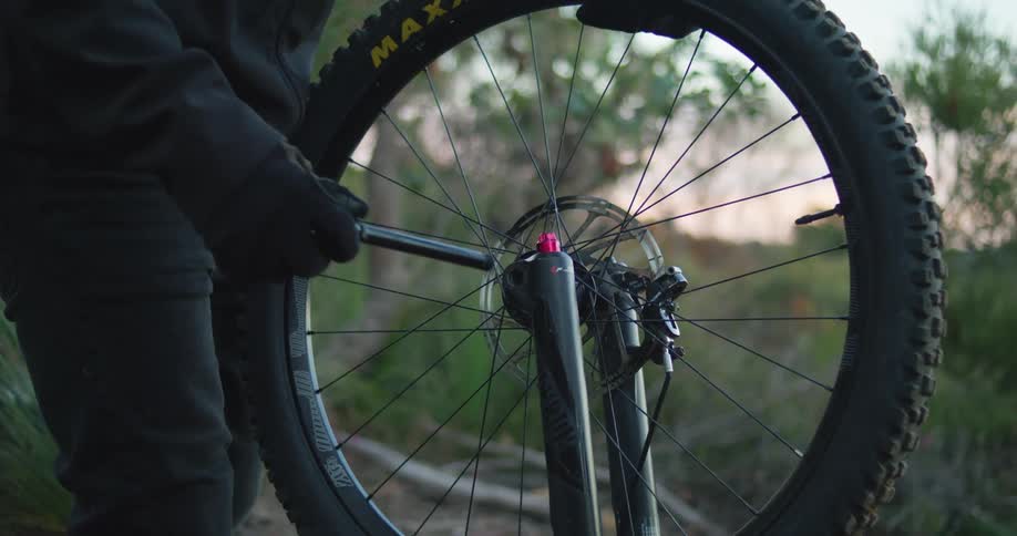 A person places a wheel on a bike frame and uses a tool to tighten it