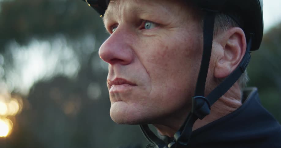 A man buckles his bicycle helmet while the wind blows the trees and leaves