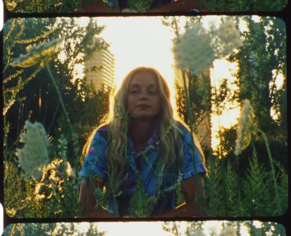 A woman sits in a garden with wildflowers with the sun glowing from behind her